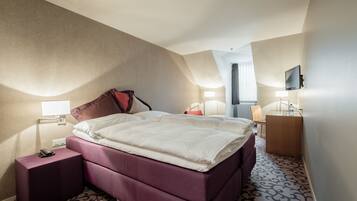 A hotel room with a large bed, a nightstand, a desk, a chair, and a television.