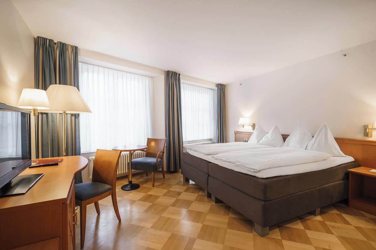 A hotel room with a bed, desk, chair, and a TV.