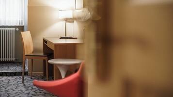 Habitación de hotel con un escritorio de madera, una silla, una mesita pequeña y un radiador.
