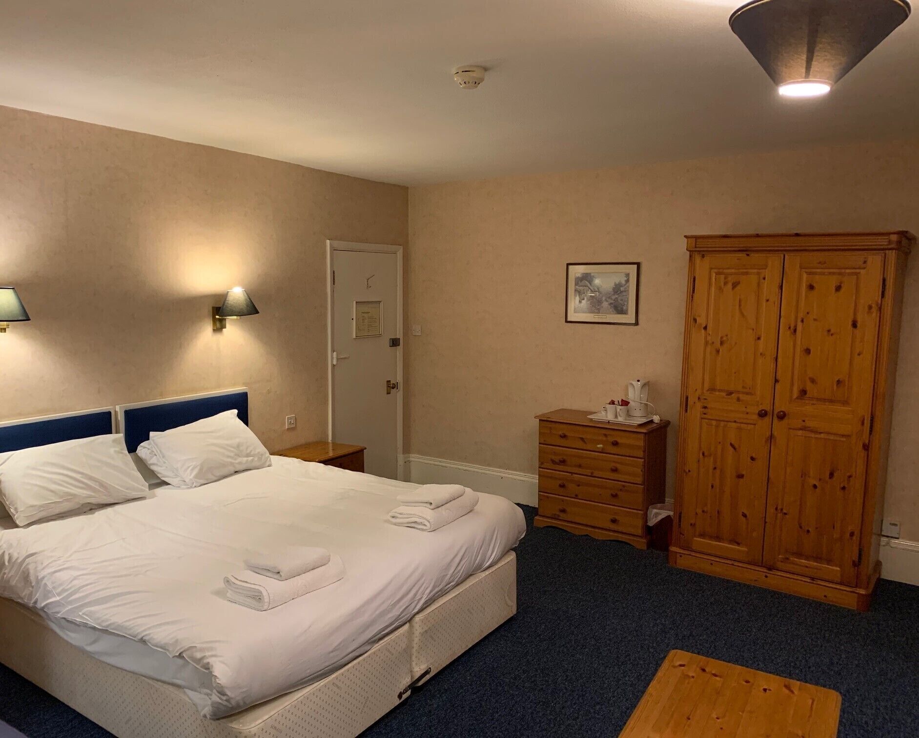 Habitación de hotel con una cama, un armario de madera, una cómoda pequeña de madera y una puerta.