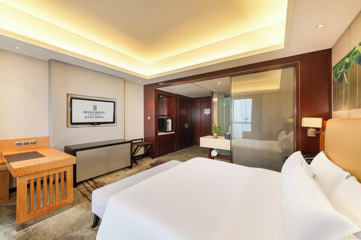 Ein Hotelzimmer mit Bett, Schreibtisch, Spiegel und Fernseher.