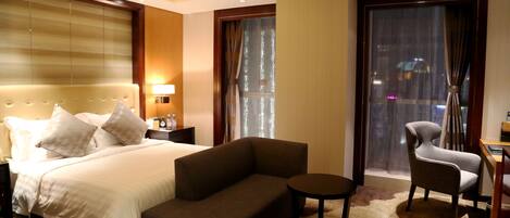 A hotel room with a bed, a sofa, a chair, a small table, and a large window with curtains.