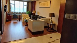 Una habitación de hotel con sofá, una mesita, lámpara, televisor y un ventanal grande.