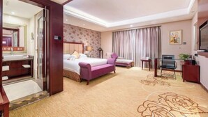 Habitación de hotel con cama, sofá, televisión, escritorio y baño visible a través de una puerta abierta.