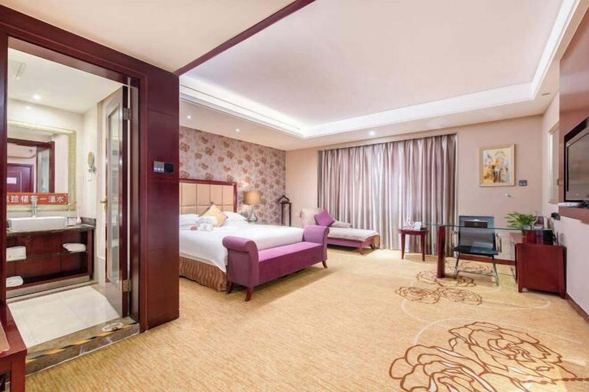 Une chambre d’hôtel avec un lit, un canapé, une télévision, un bureau et une salle de bain visible à travers une porte ouverte.