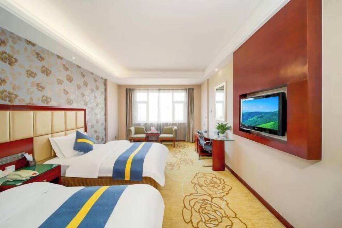 Une chambre d’hôtel avec deux lits, un bureau, une télévision et une vue sur un paysage par la fenêtre.