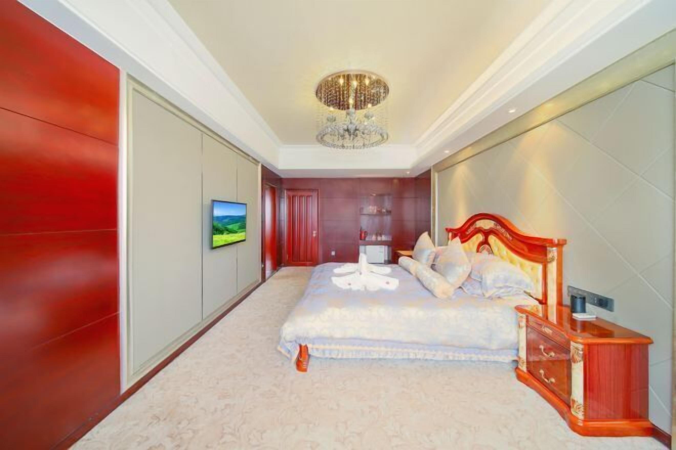 Ein Schlafzimmer mit einem großen Bett, einer Kristallleuchter, einem Fernseher und einer roten Akzentwand.