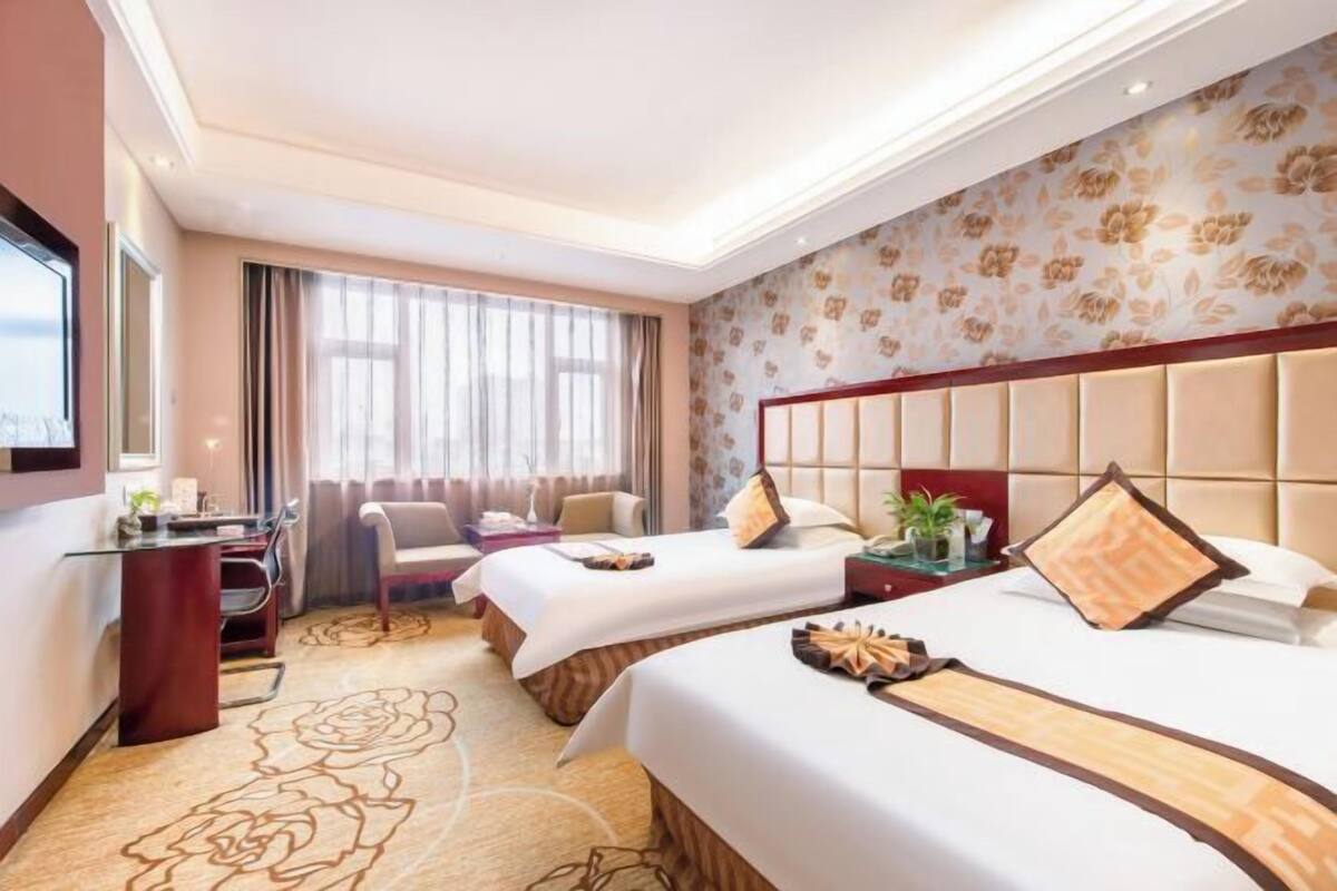 Une chambre d’hôtel avec deux lits, un bureau, une chaise et une grande fenêtre avec des rideaux.