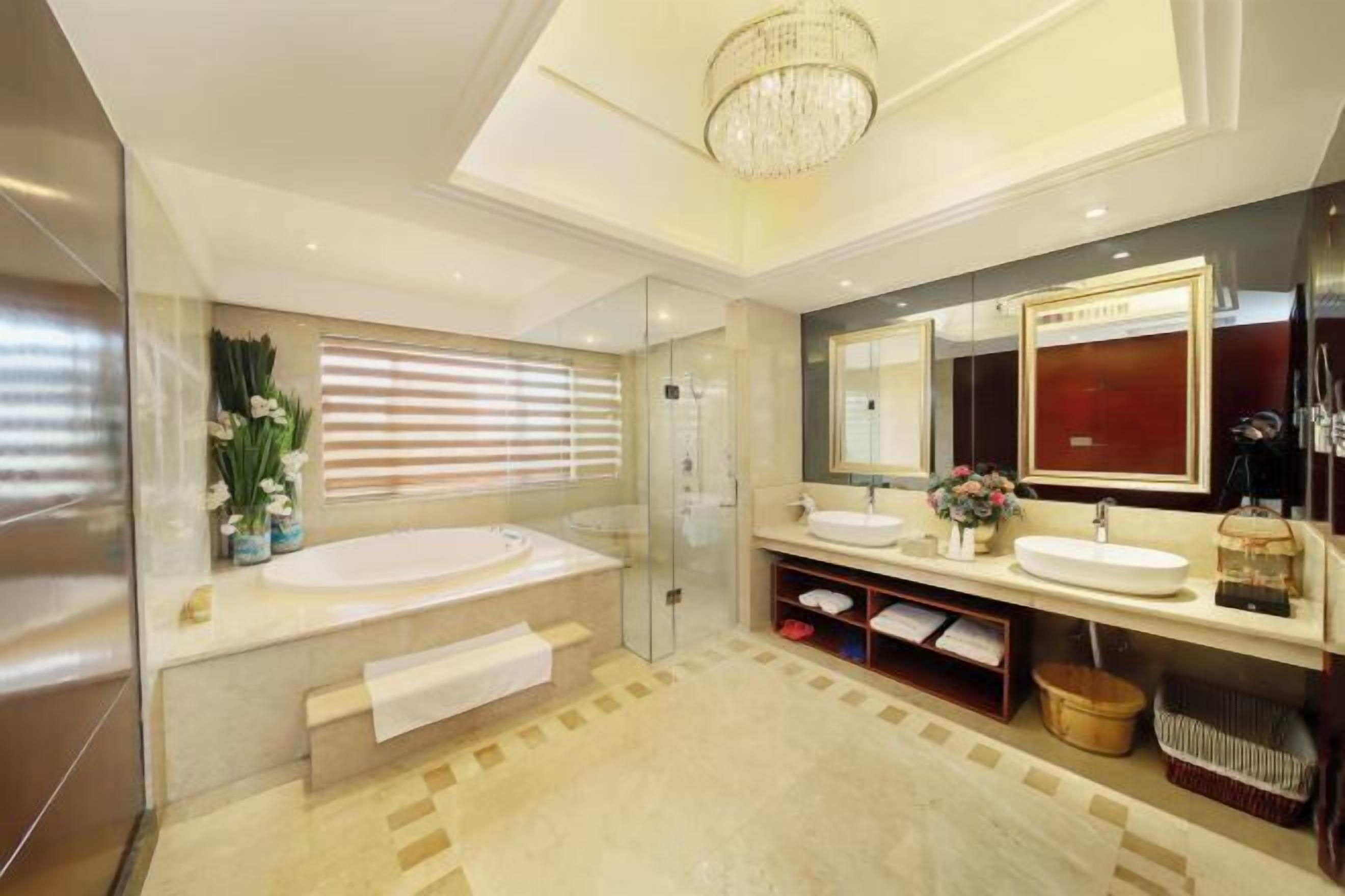 Ein modernes Badezimmer mit Badewanne, zwei Waschbecken, einem großen Spiegel und einer Chandelier.
