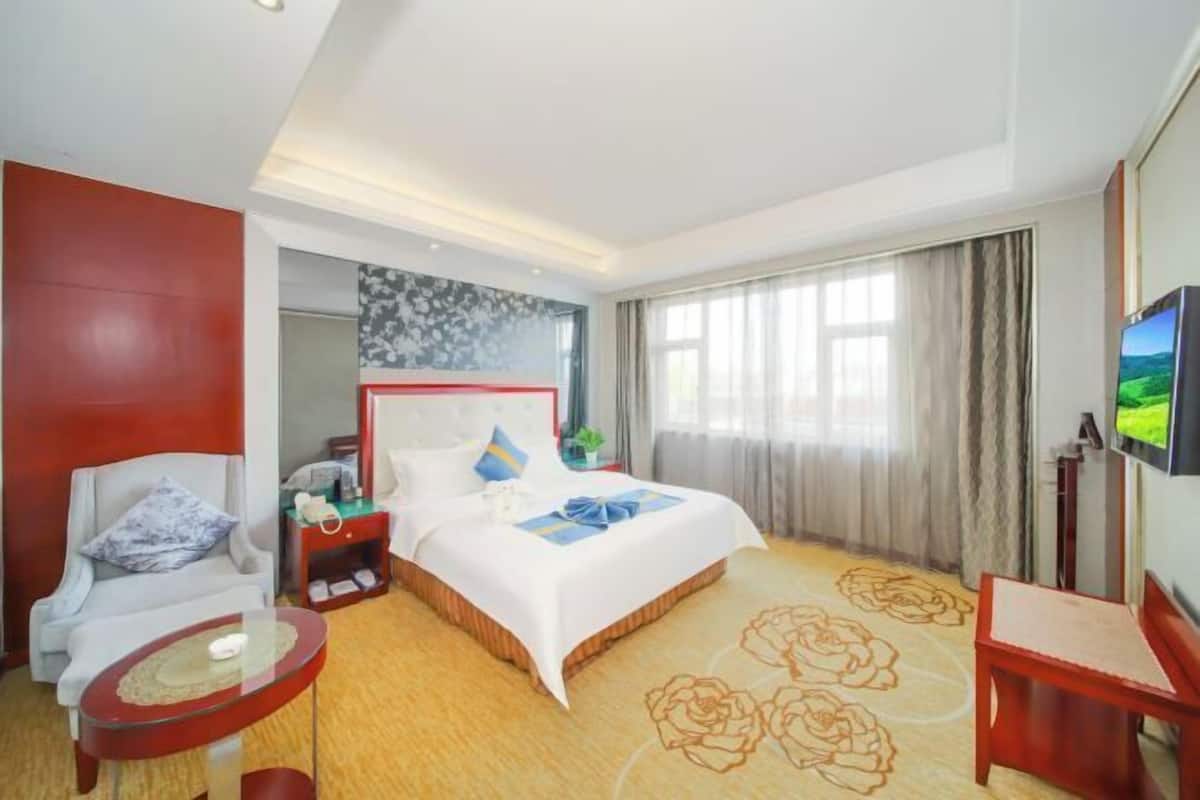 Une chambre d’hôtel avec un lit, une chaise, une petite table, un téléviseur et une fenêtre avec des rideaux.