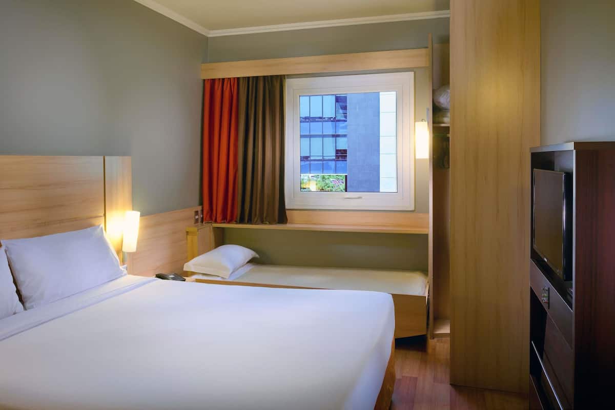 A hotel room with a large bed, a TV, a window with curtains, and a small table.