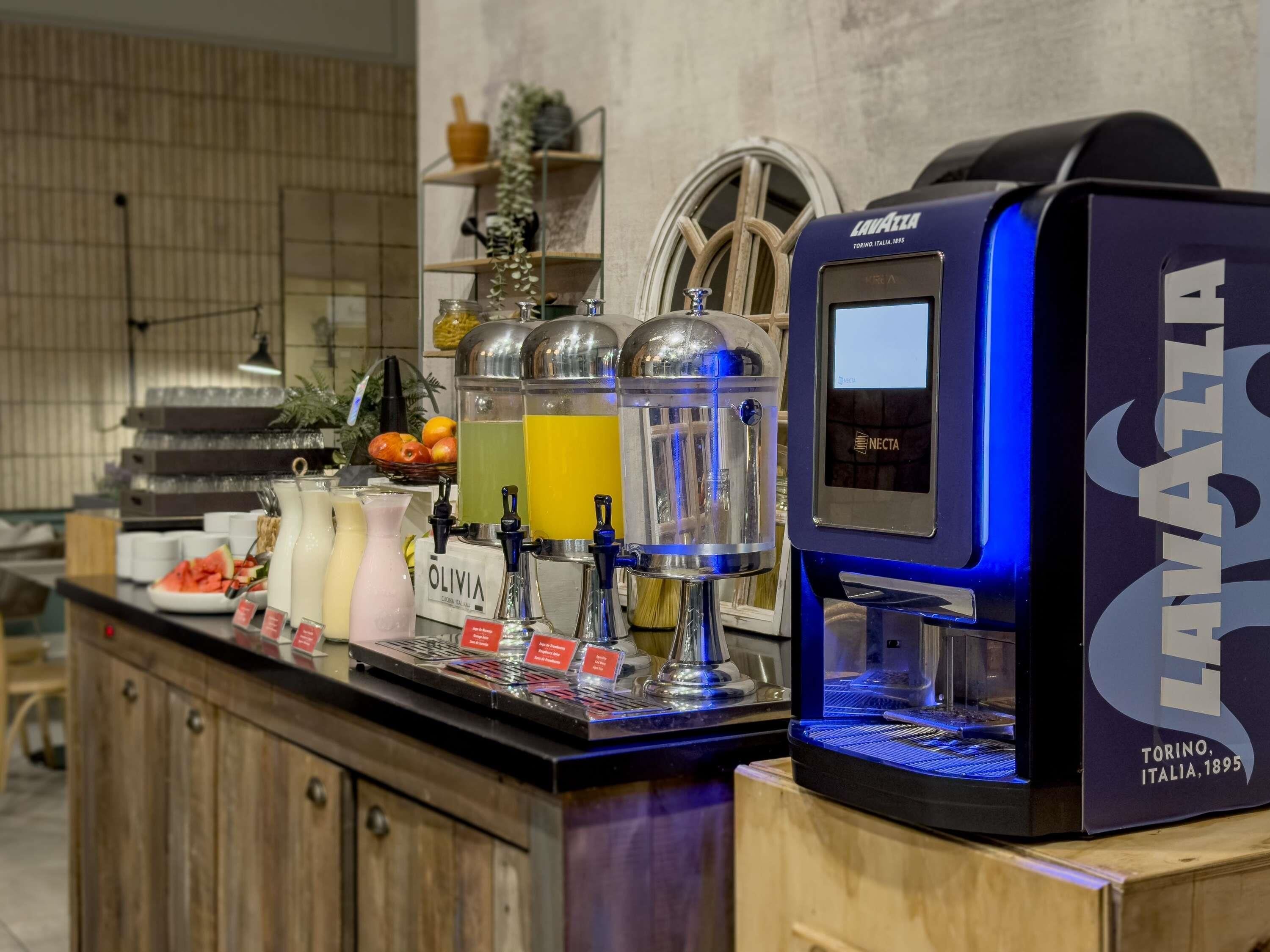 Zona de bar con una máquina de café, varios dispensadores de bebidas y una exhibición de frutas.