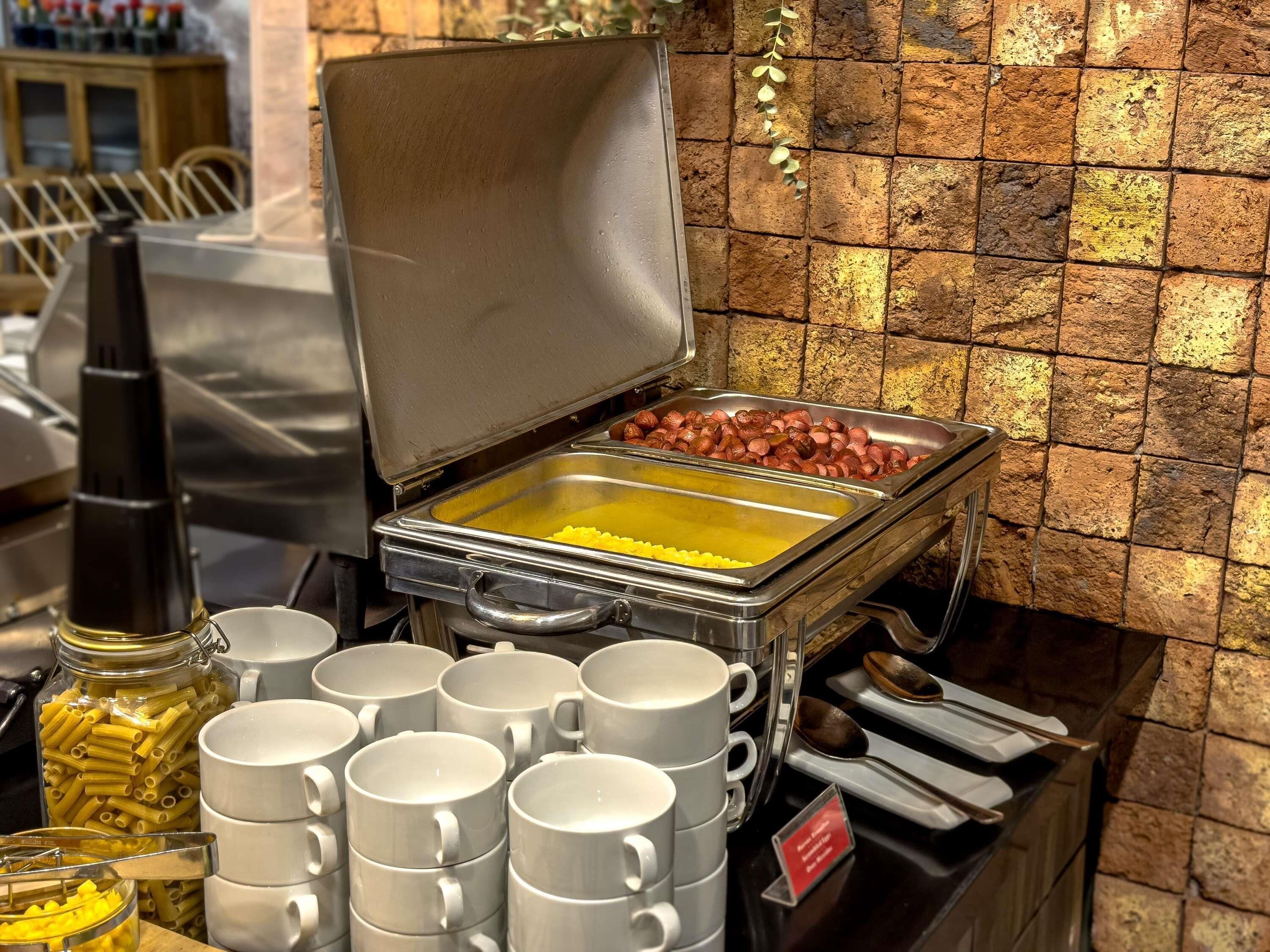A buffet setup with pasta, sausages, and a coffee station.