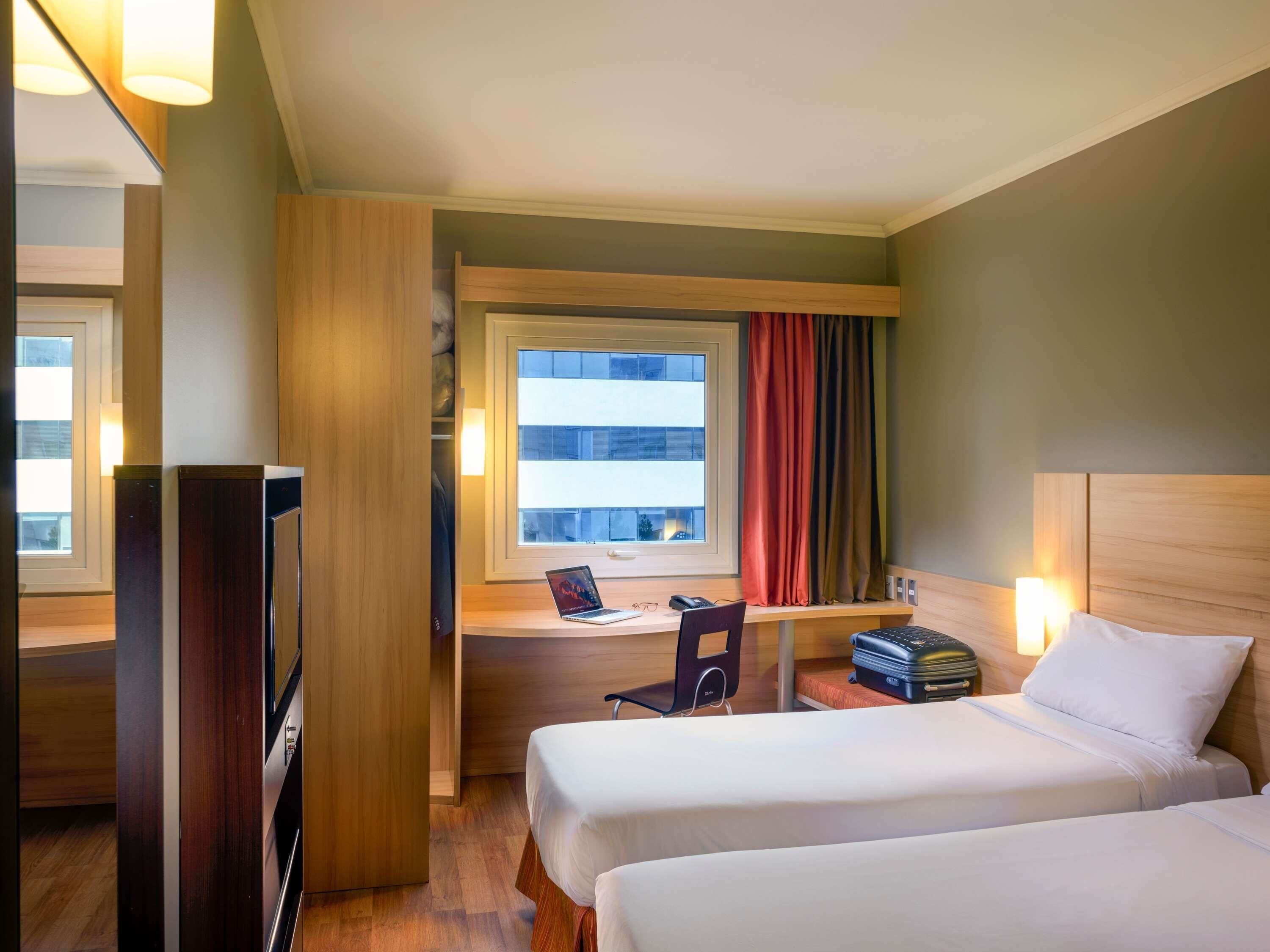 Habitación de hotel con dos camas, un escritorio con una computadora portátil, una silla y un televisor.