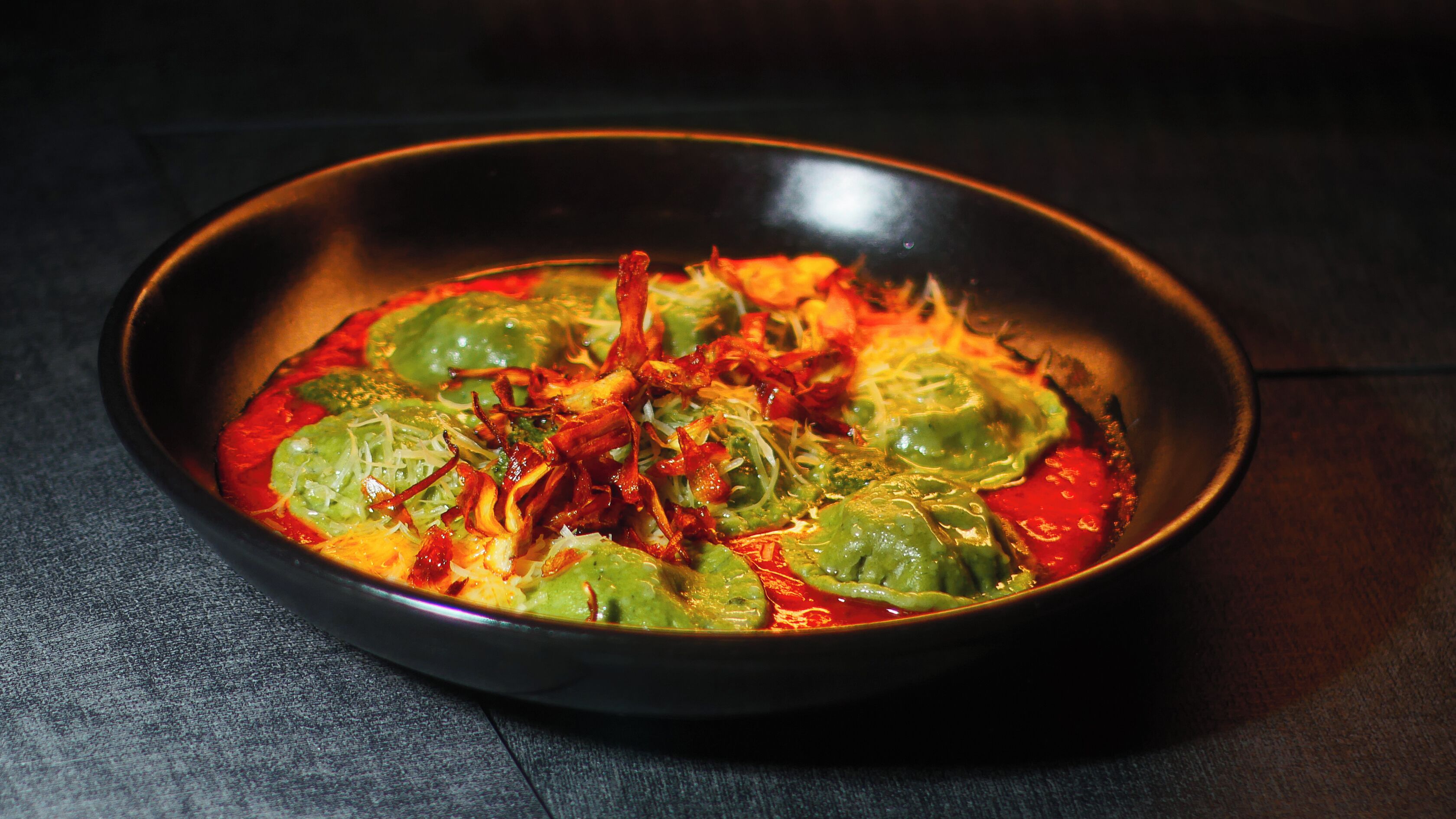 Un plato de comida con elementos verdes y rojos, posiblemente un guiso de verduras y carne, sobre una superficie oscura.