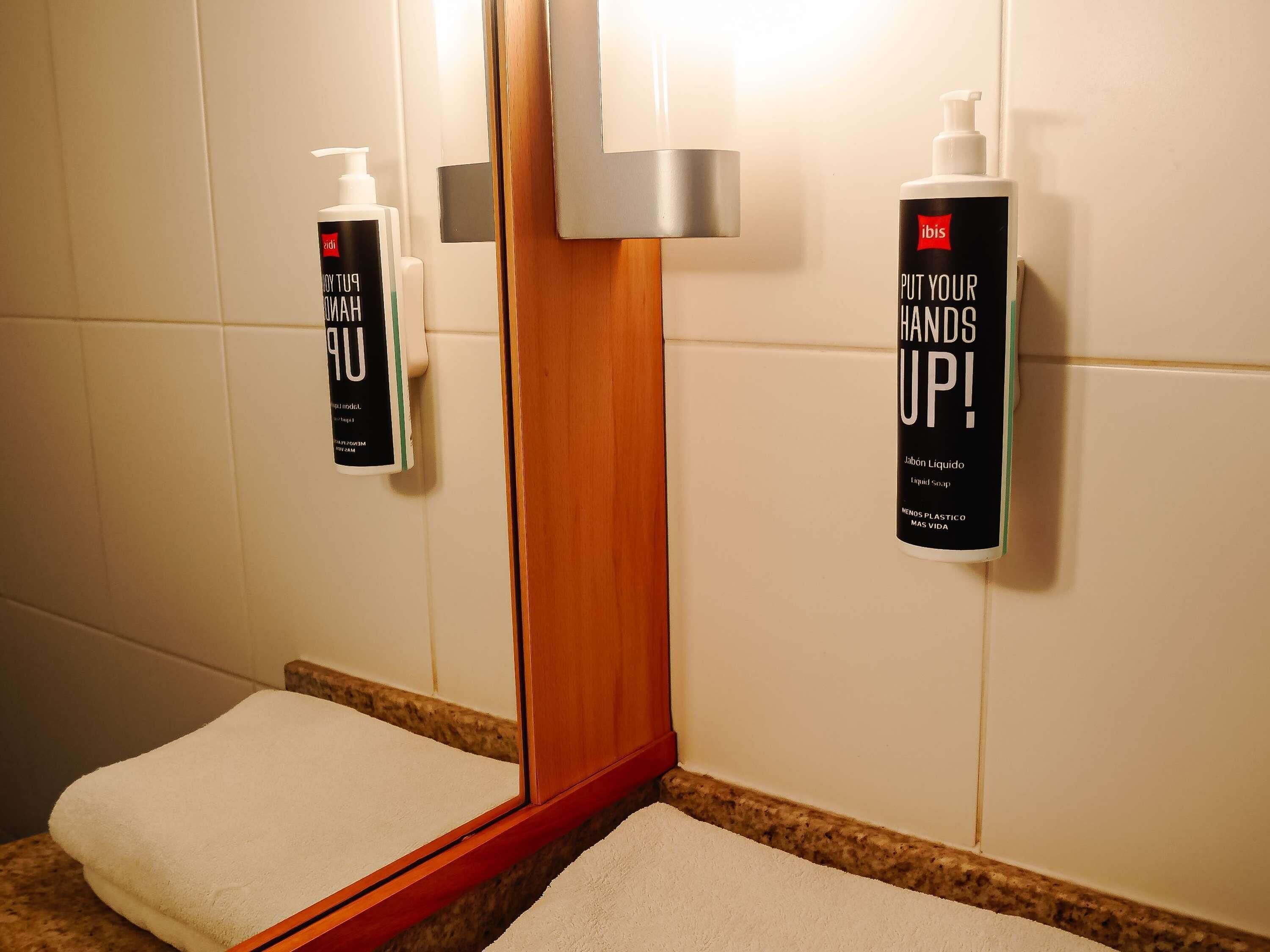 A bathroom with a mirror, two hand sanitizer dispensers, and a towel on the floor.