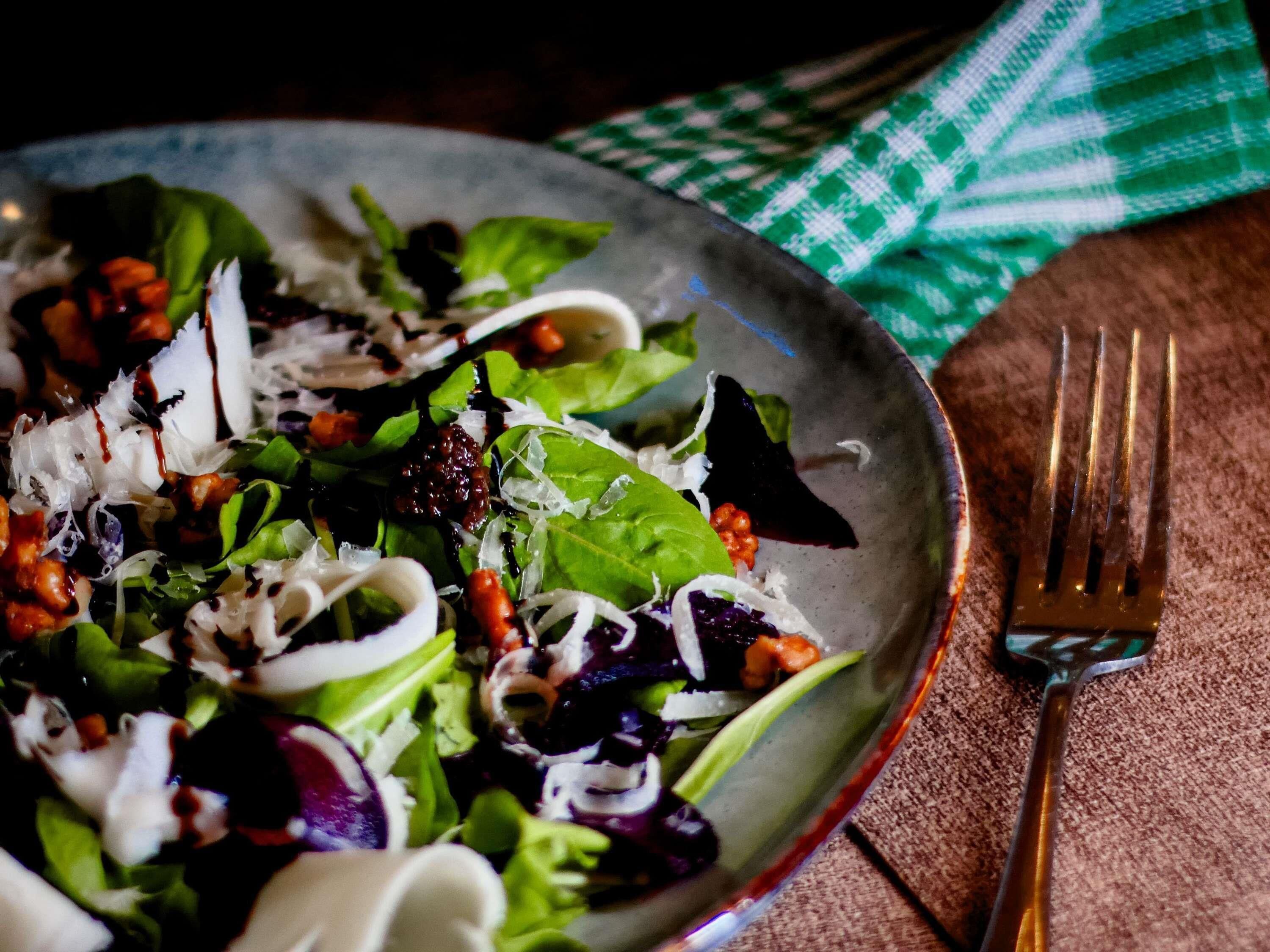 Un'insalata in una ciotola, con diverse verdure e condimenti, una forchetta accanto e un tovagliolo a quadretti verdi e bianchi sul tavolo.