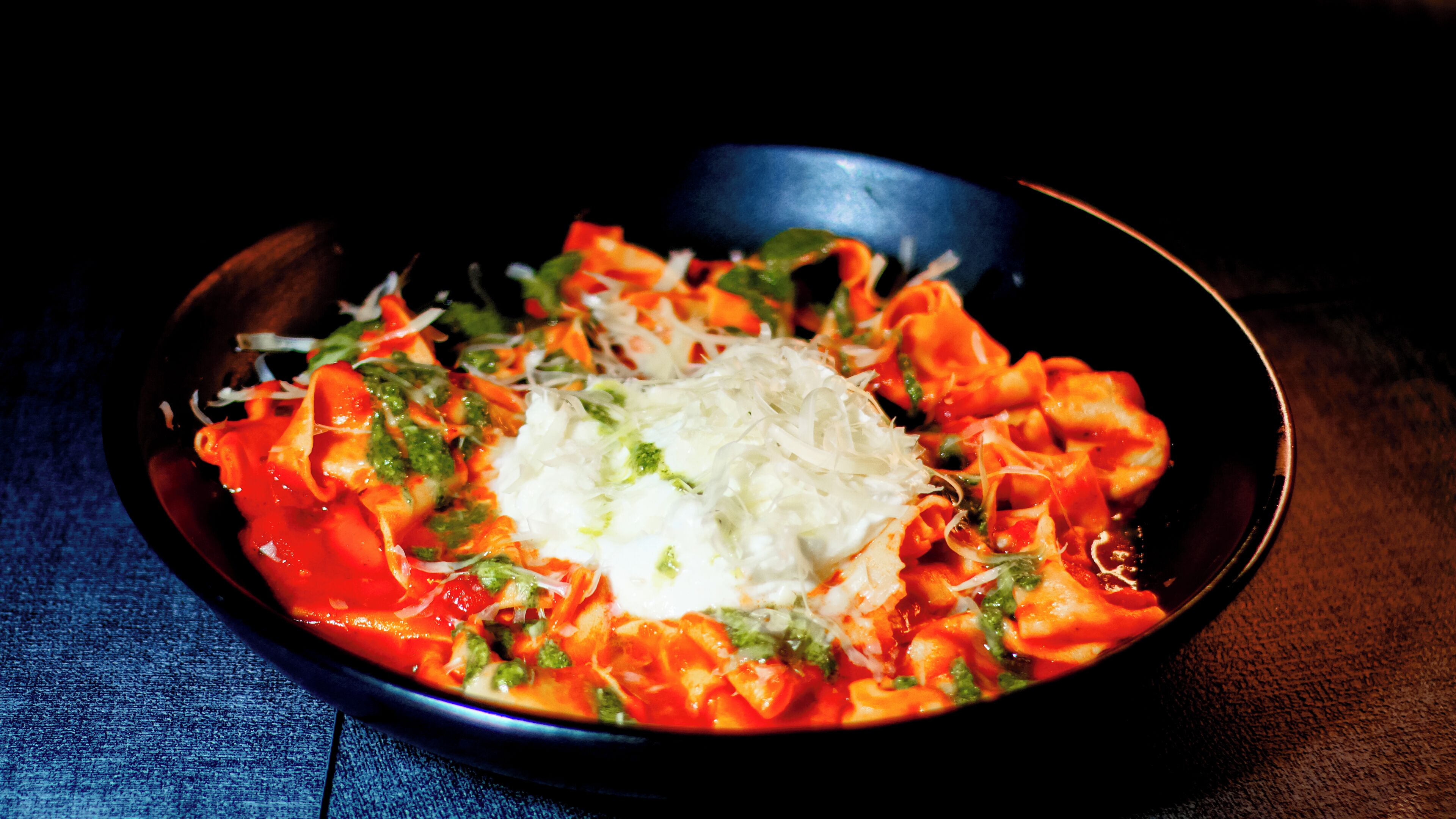 A bowl of pasta with tomato sauce, cheese, and herbs.