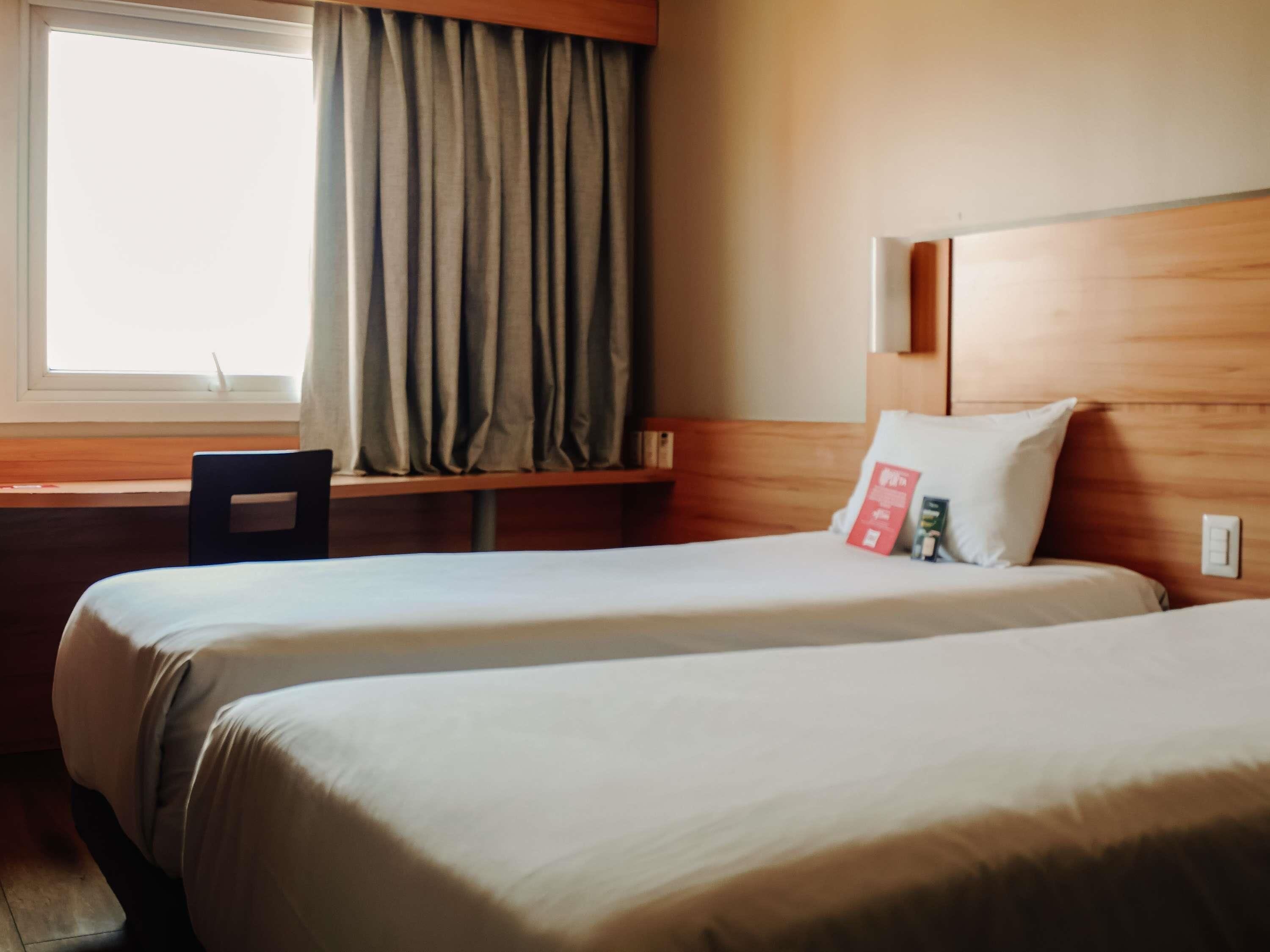 Habitación de hotel con dos camas, un escritorio, una silla y una ventana con cortinas.