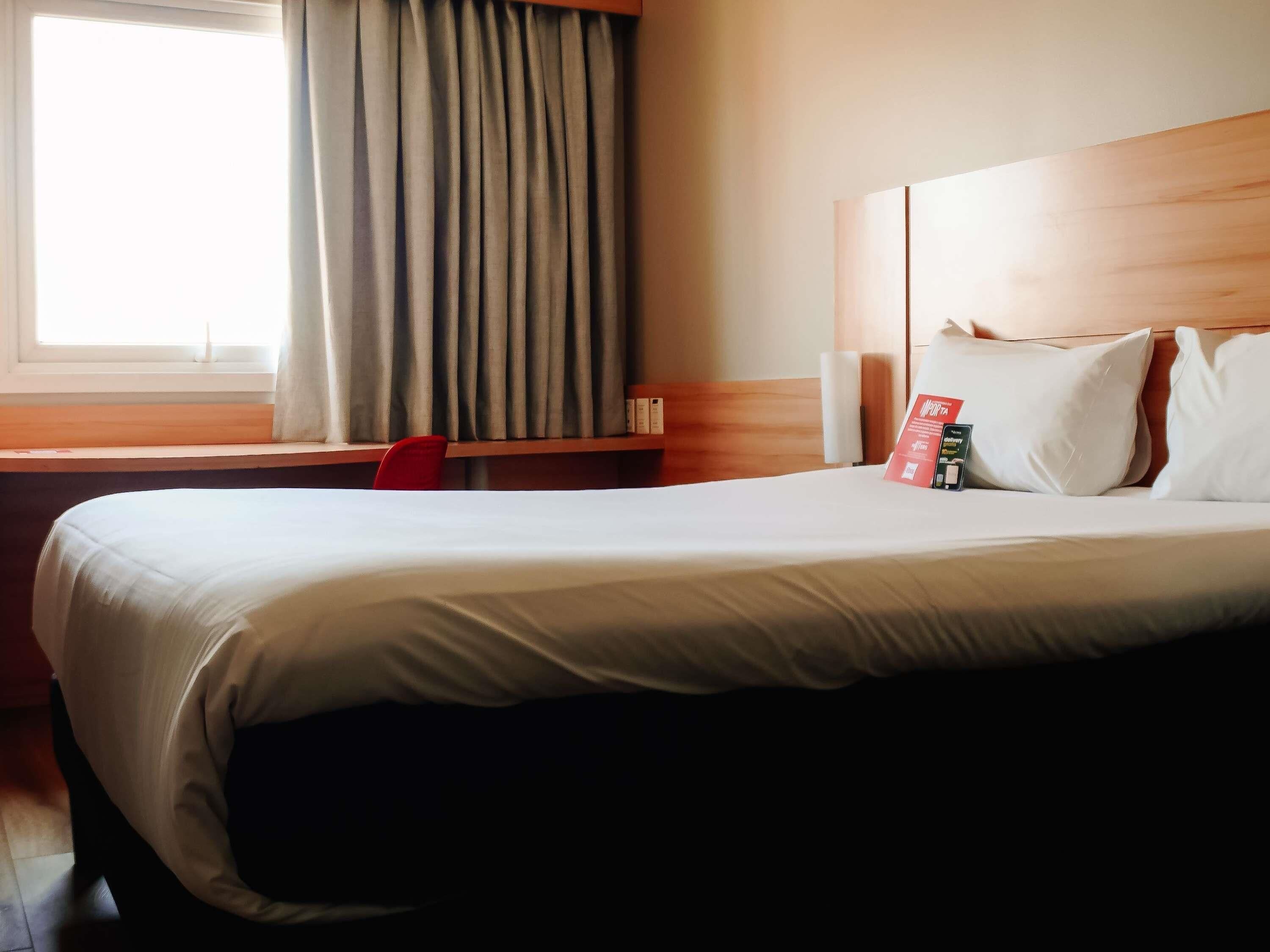 A hotel room with a bed, a desk, a chair, and a window with curtains.