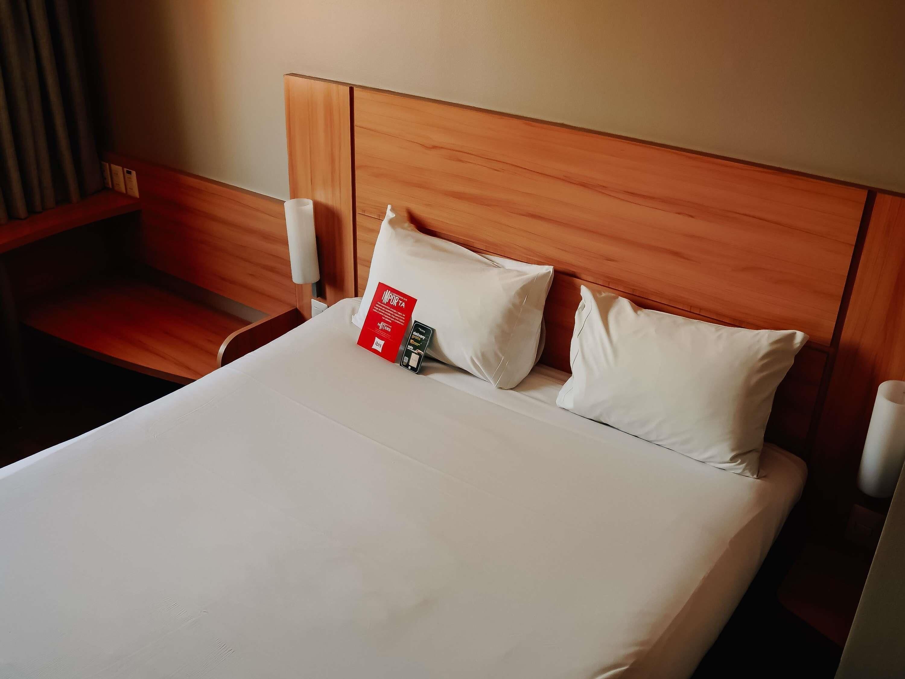 Habitación de hotel con cabecera de madera, cubrecama blanco y dos almohadas blancas.