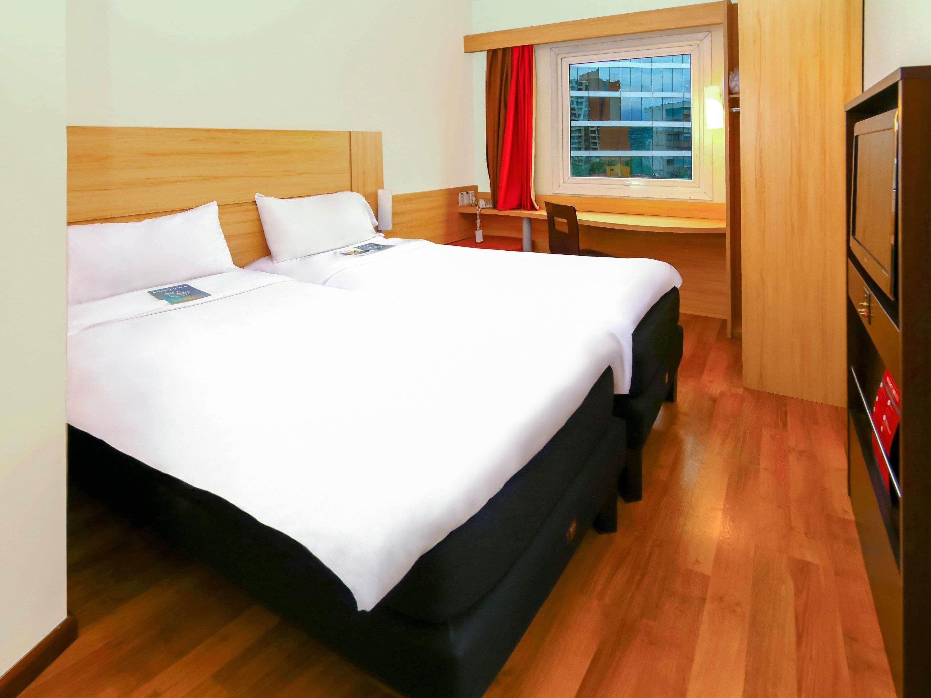 A double bed with white linens, a wooden headboard, and a wooden floor.