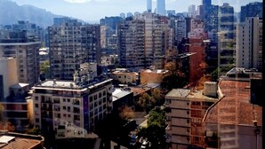 Une vue urbaine avec un gratte-ciel imposant, des immeubles résidentiels et une chaîne de montagnes en arrière-plan.