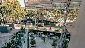 Un café moderno al aire libre con barandillas de vidrio, plantas en macetas y mesas.