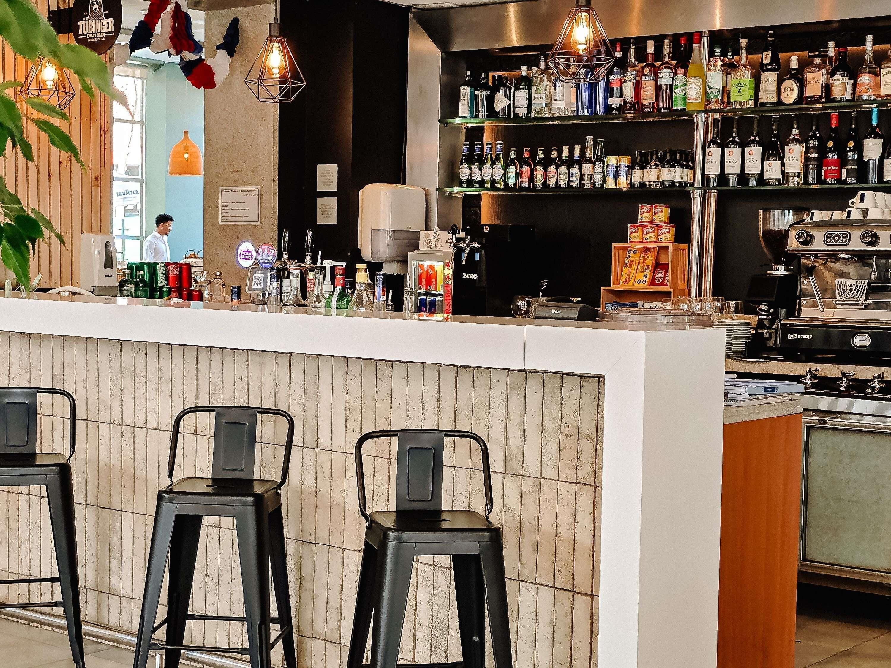 A bar area with stools, a variety of liquor bottles, and a coffee machine.