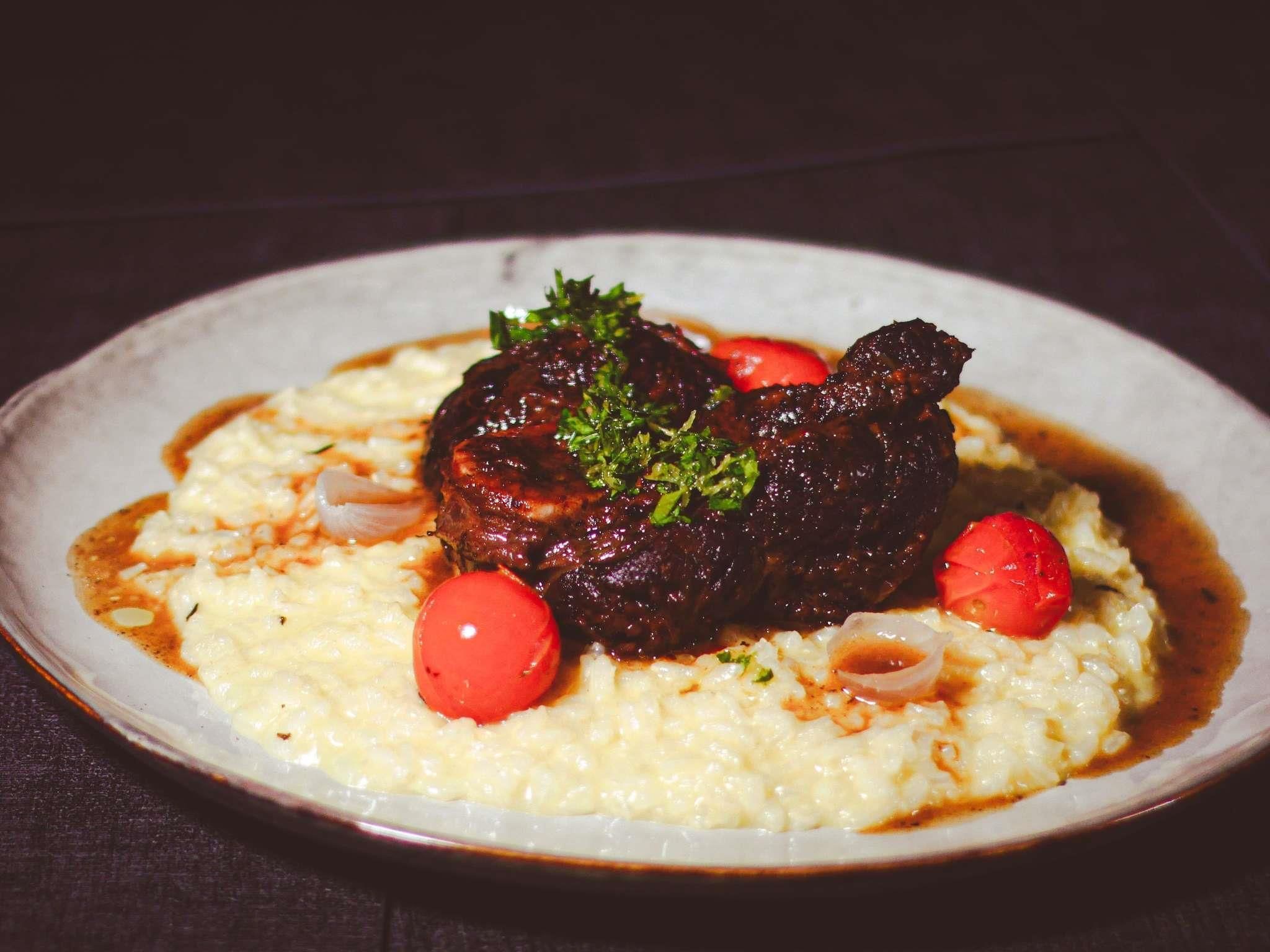 Un plato con un guiso de carne, puré de papas y un tomate cherry como adorno.