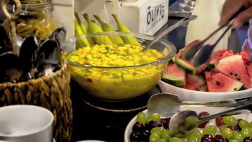 Un bufé con diversos alimentos, incluyendo frutas, un tazón de ensalada de mango y un tazón de uvas.