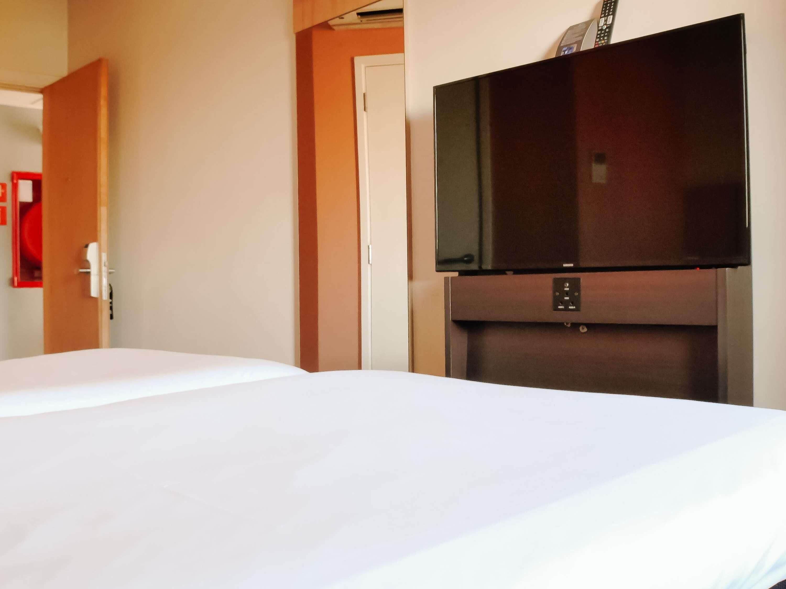 Habitación de hotel con una cama, un televisor montado en un mueble de madera y una puerta que da a otra habitación.