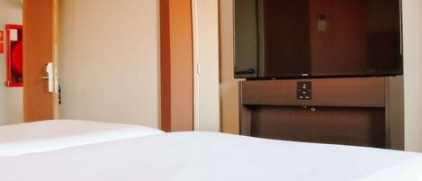 Habitación de hotel con una cama, un televisor montado en un mueble de madera y una puerta que da a otra habitación.