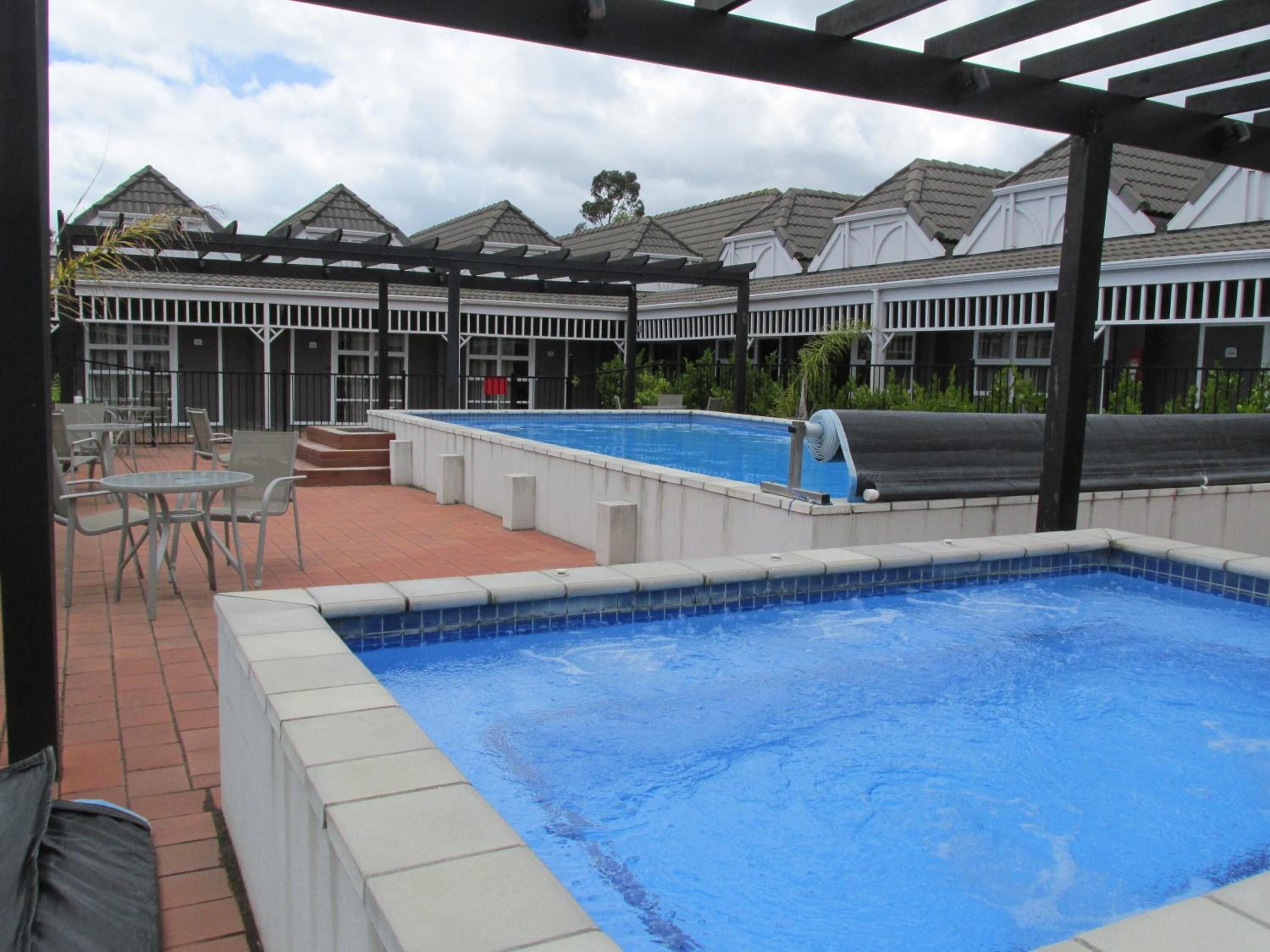 Una piscina con pérgola y zona de estar al aire libre, rodeada de edificios con un estilo arquitectónico uniforme.