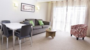 A modern living room with a grey sofa, a dining table with chairs, a patterned armchair, and a framed artwork on the wall. - Lake Rotorua Hotel (Rotorua)