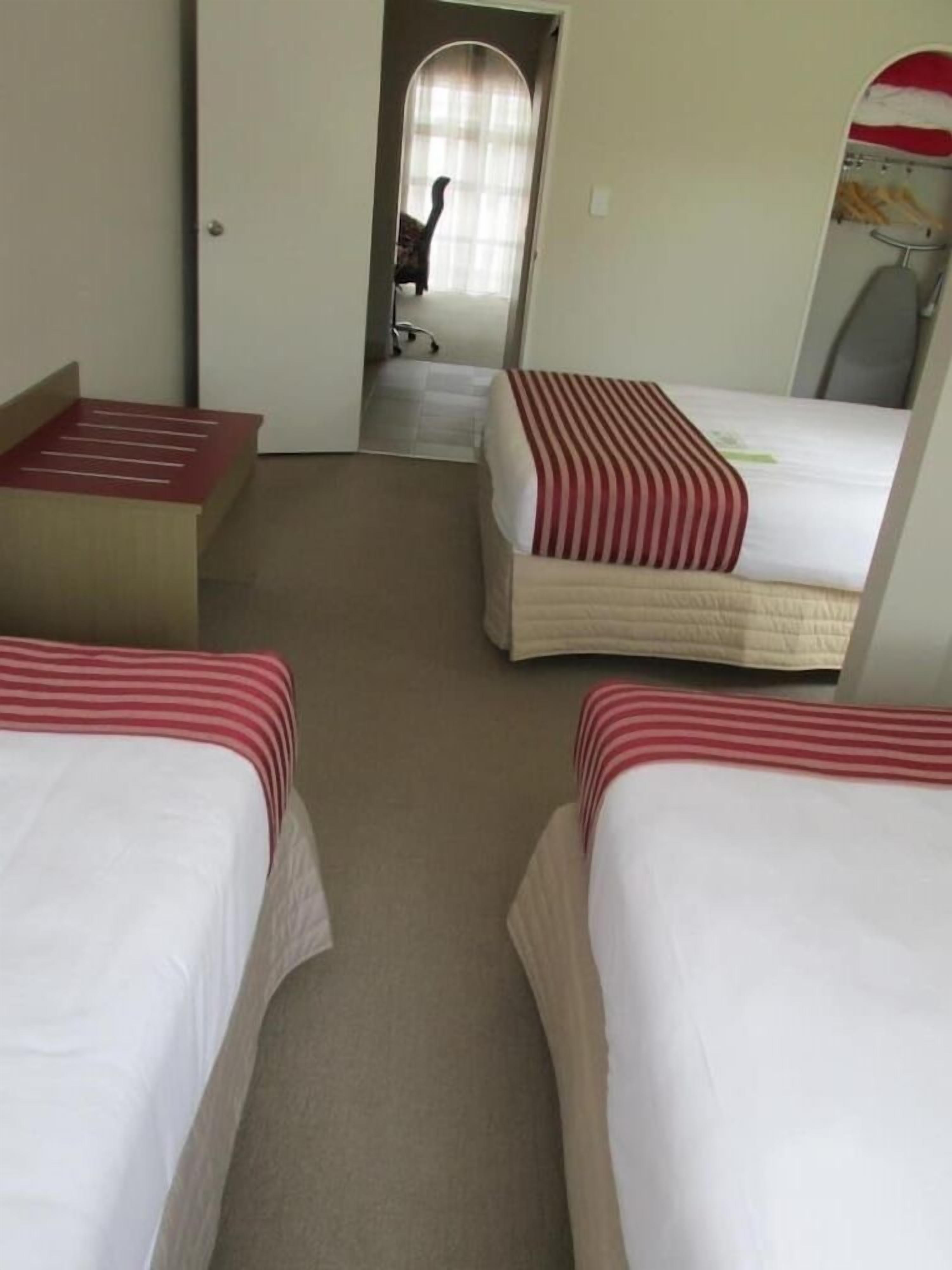 A compact hotel room with bunk beds, a small bathroom with a mirror, and a window with curtains.