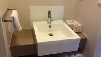 A bathroom with a white sink, a towel rack, and a shelf with rolled towels.