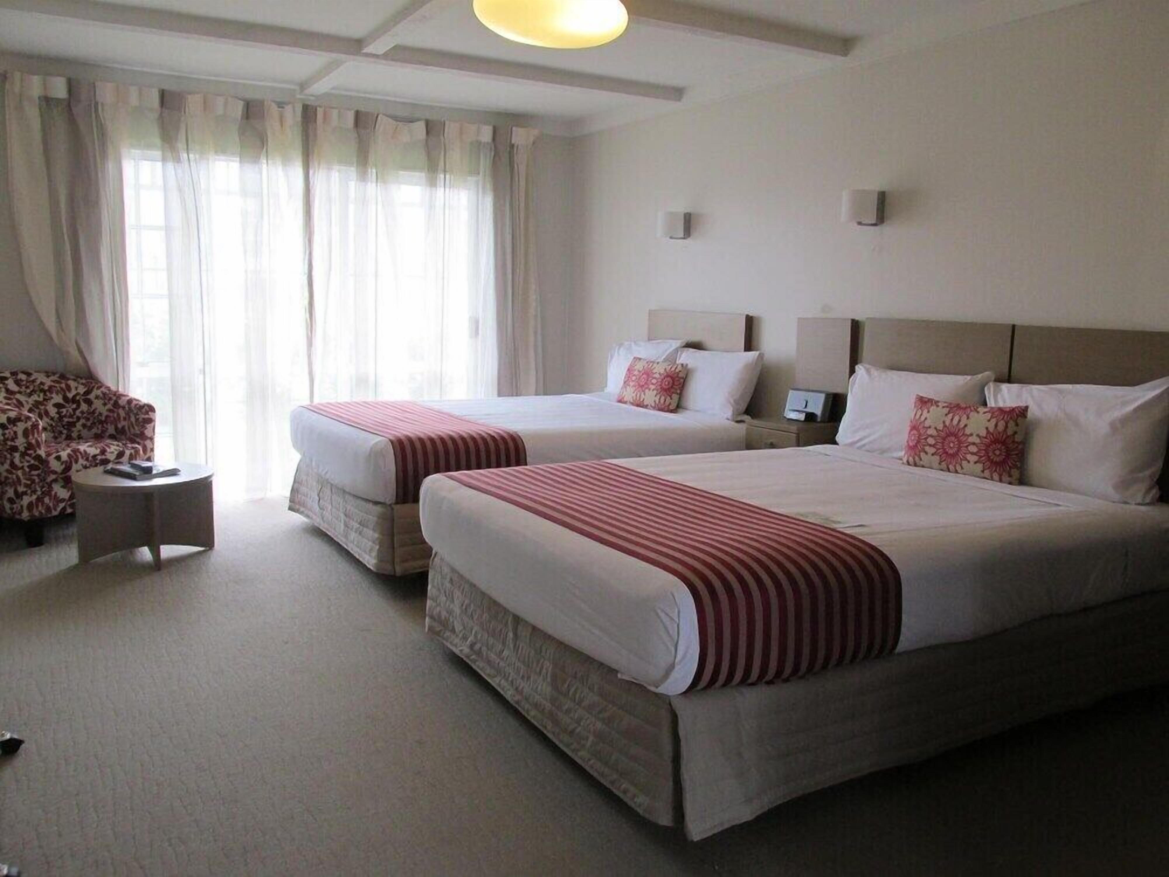 A hotel room with two beds, a sofa, a small table, and a window with curtains.