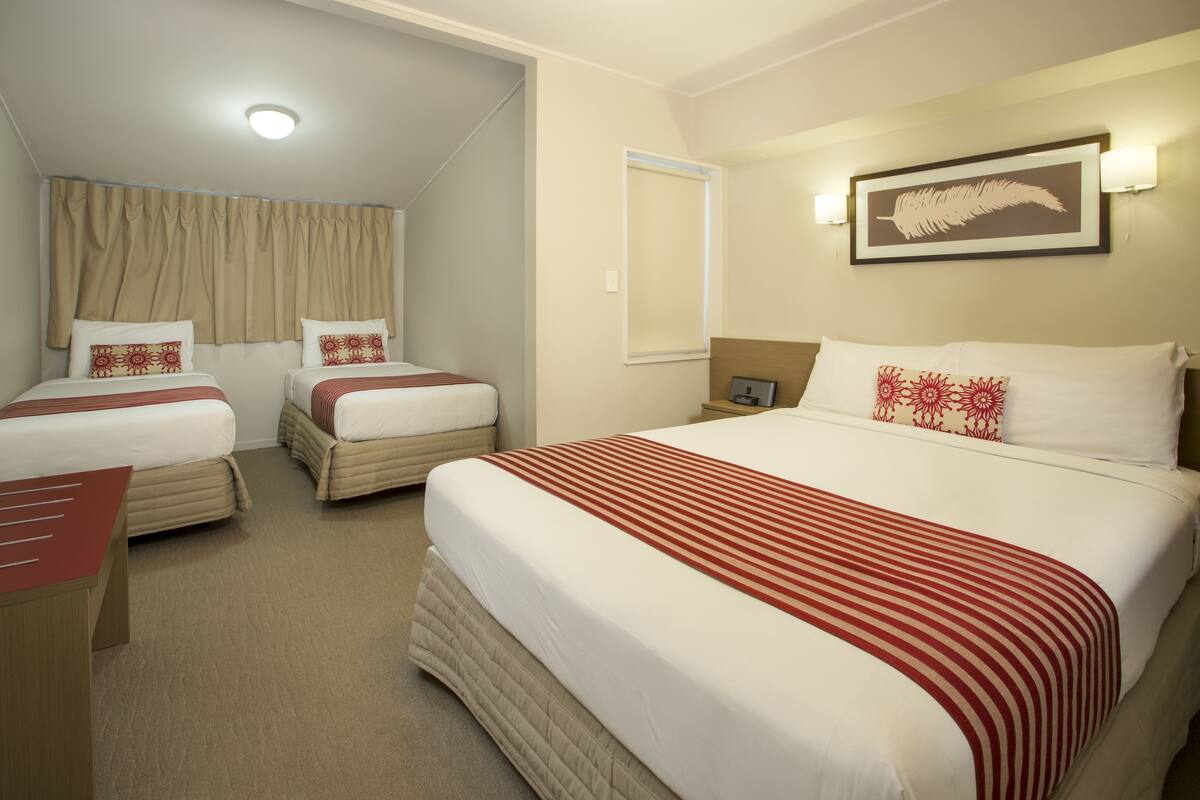 Quarto de hotel com duas camas de solteiro, uma cama maior, uma escrivaninha e uma cadeira.