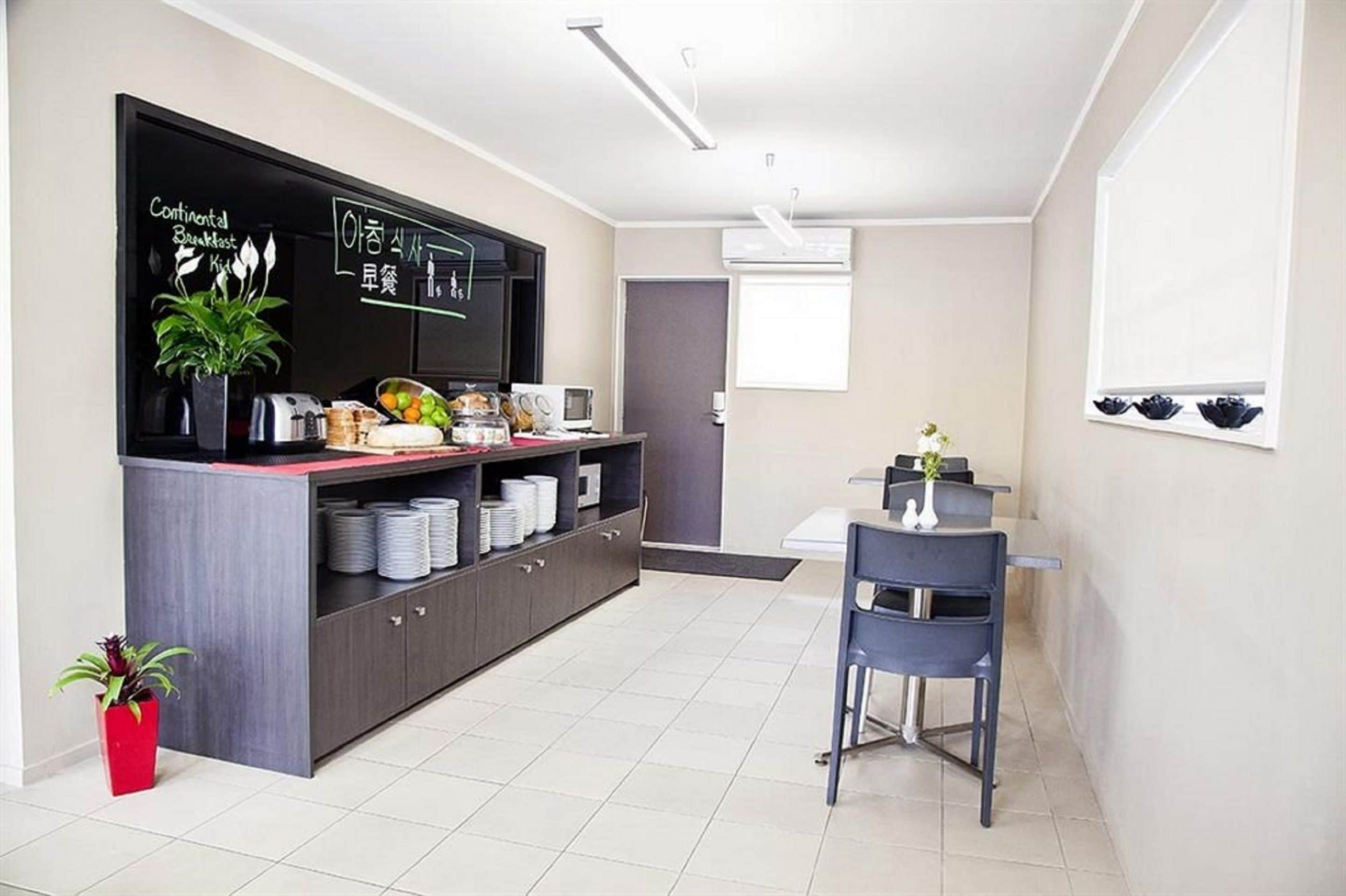 Une cuisine moderne avec un tableau noir affichant les options de petit-déjeuner, une table à manger avec des chaises et une plante en pot.