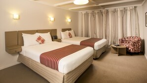 A hotel room with two beds, a small table, a chair, and a window with curtains. - Lake Rotorua Hotel (Rotorua)