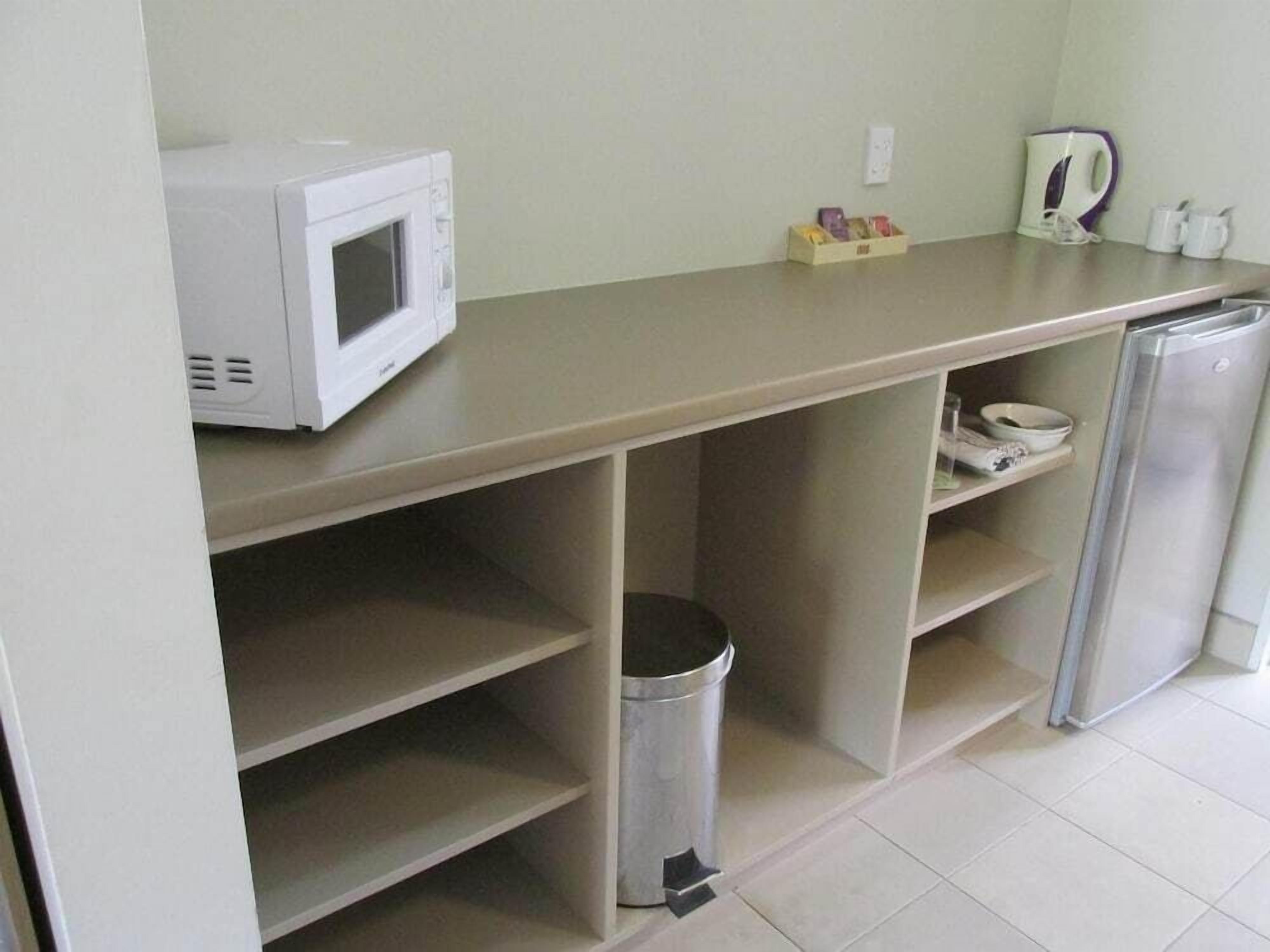Een kitchenette met een magnetron, waterkoker en een afvalbak.