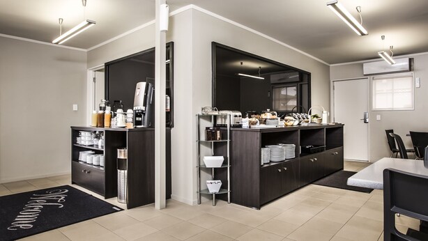 A modern kitchen with dark cabinetry, a built-in coffee station, and a large mirror. - Lake Rotorua Hotel (Rotorua)