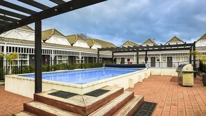 A swimming pool with steps leading into it, surrounded by a covered patio area with a grill and a view of a row of houses. - Lake Rotorua Hotel (Rotorua)