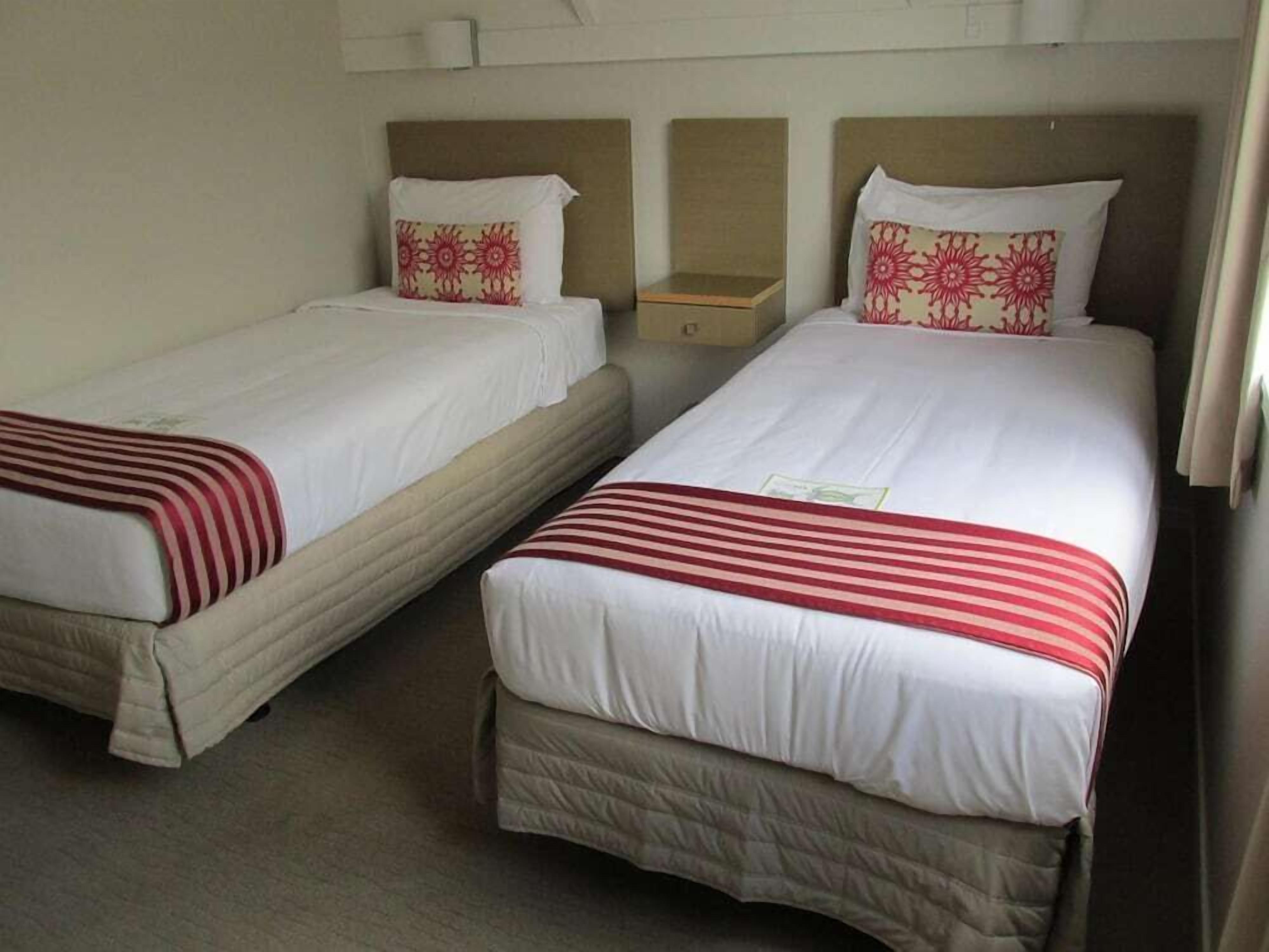 Two single beds with white bedding and red and white striped blankets, a wooden nightstand, and a beige carpet.