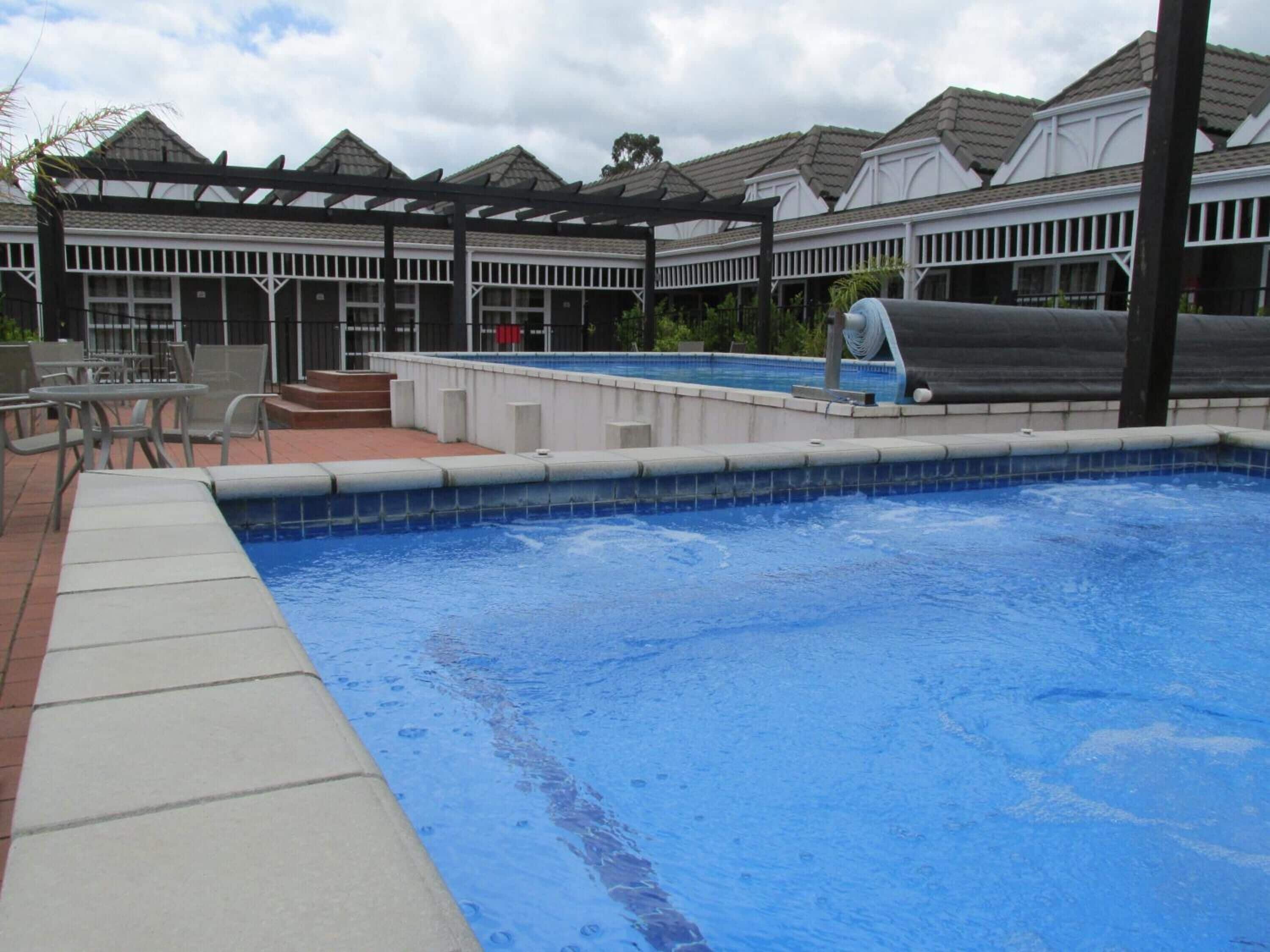 A swimming pool with a tiled edge, a water feature, and a pergola structure.