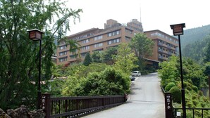 Un immeuble à plusieurs étages doté d’une architecture moderne, entouré d’une végétation luxuriante et accessible par un pont.