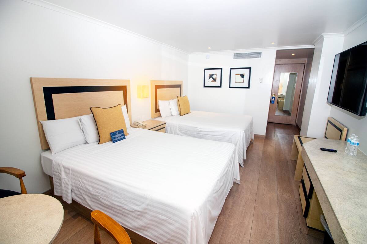 A hotel room with two beds, a desk, a chair, and a television.