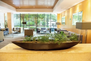 Un'elegante hall moderna con un grande vaso di piante, posti a sedere confortevoli e ampie finestre che si affacciano sul verde.