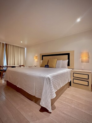 A hotel room with a large bed, bedside tables, a desk, and a chair.